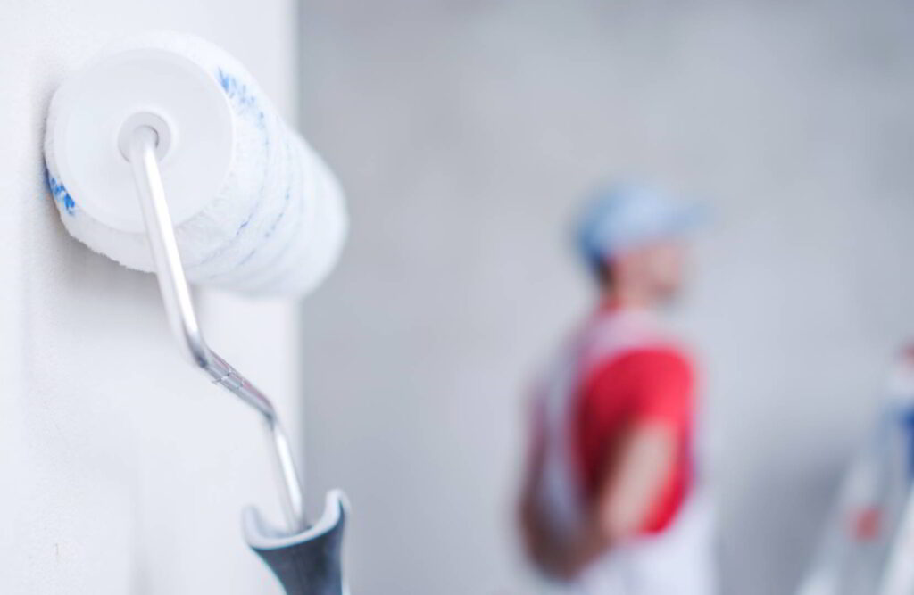 Interior Painting Roller and the Worker in the Background. Home Remodeling Concept.
