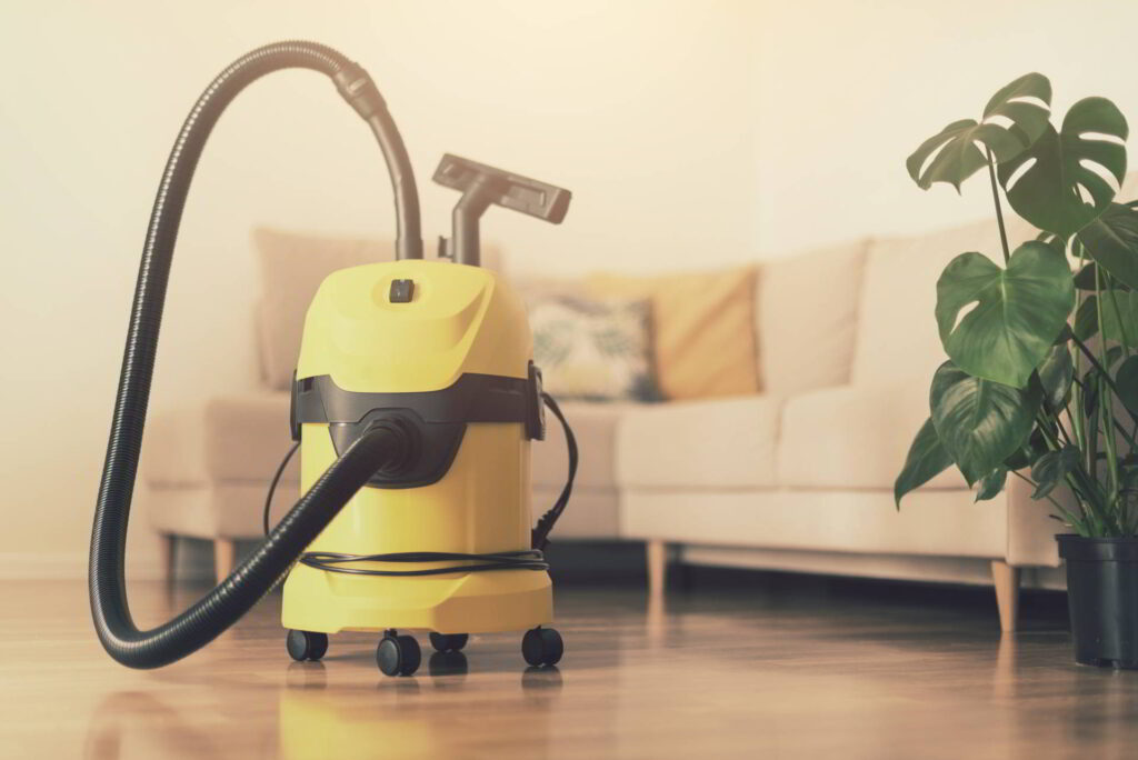 Yellow modern vacuum cleaner in living room. Copy space. Flat clean vacuuming concept. Green monstera plant.